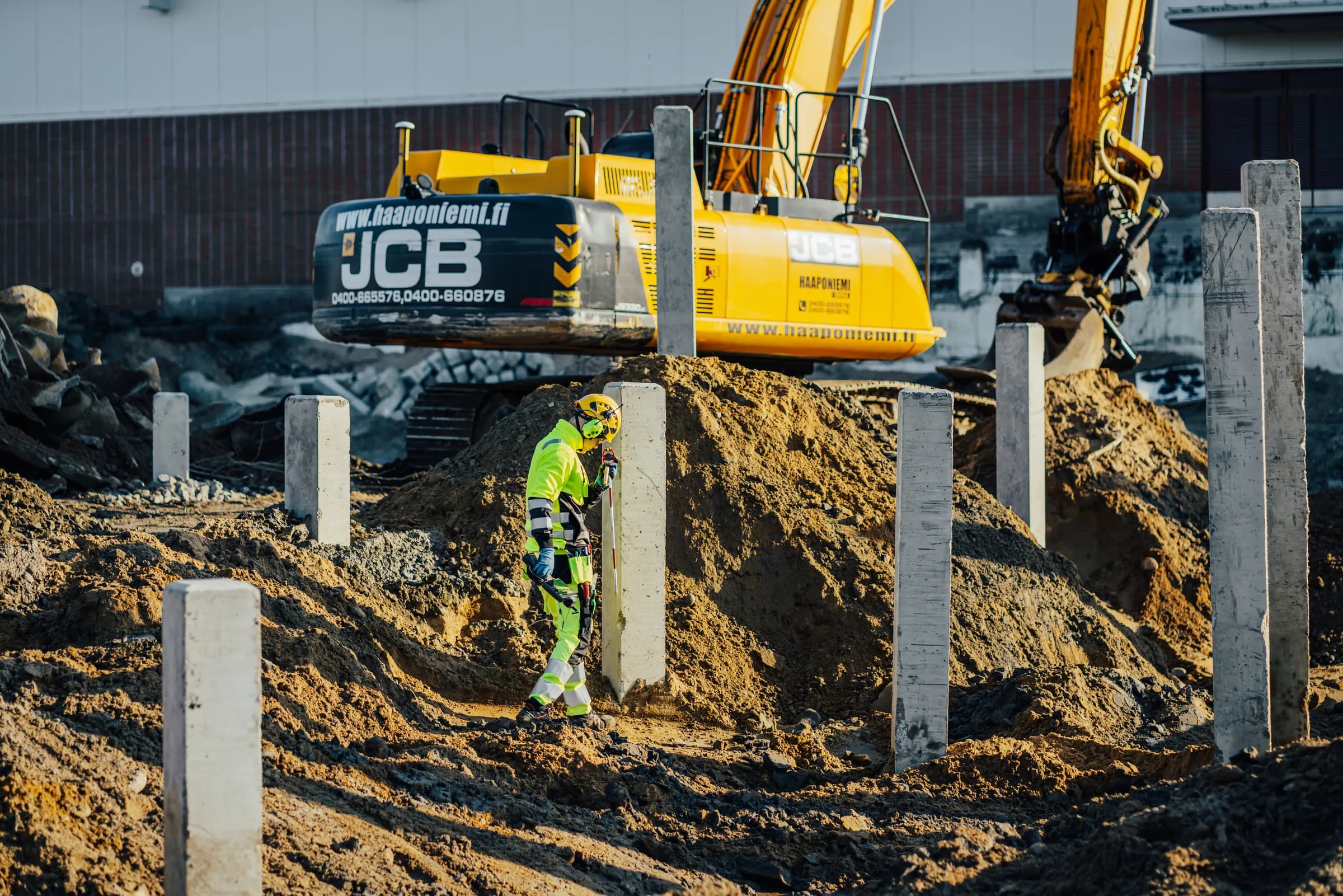Mättekniker vid betongpelare med en grävmaskin i bakgrunden
